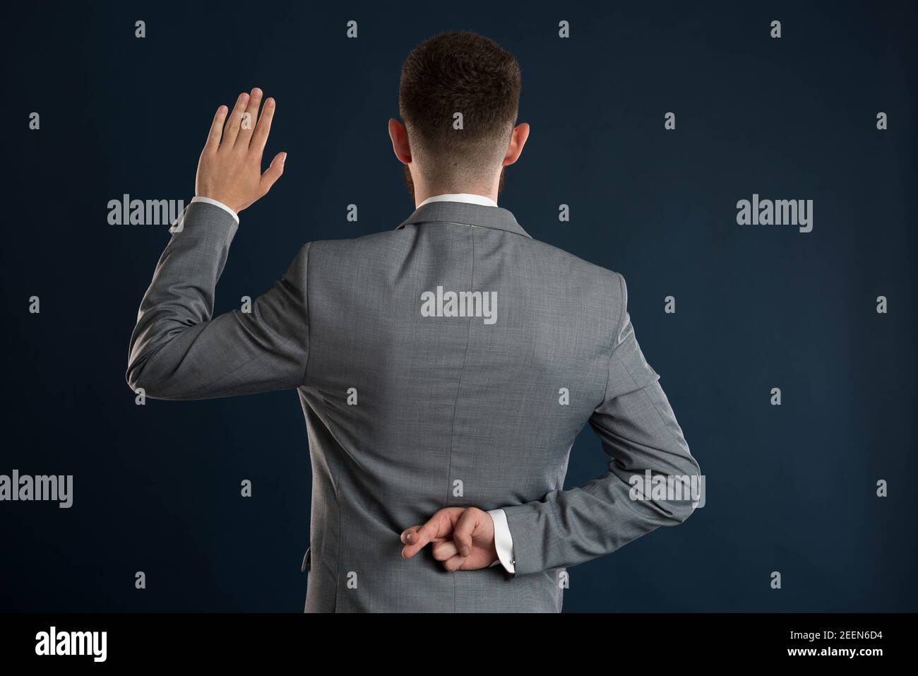 Young businessman taking a fake oath with his back to the camera wearing a grey jacket Stock Photo