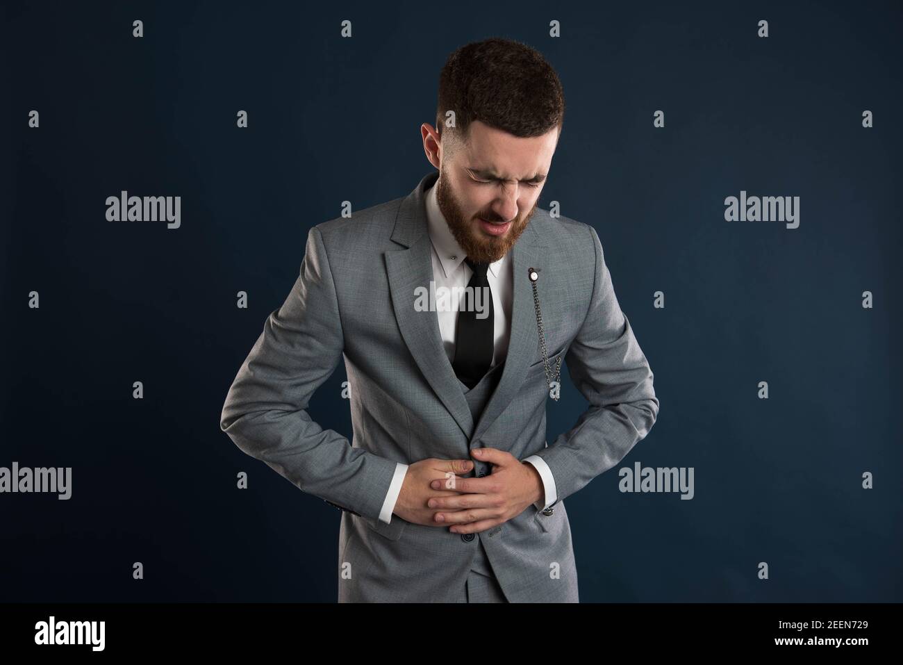 Handsome young white collar worker with abdominal pain wearing a grey suit and a black tie Stock Photo