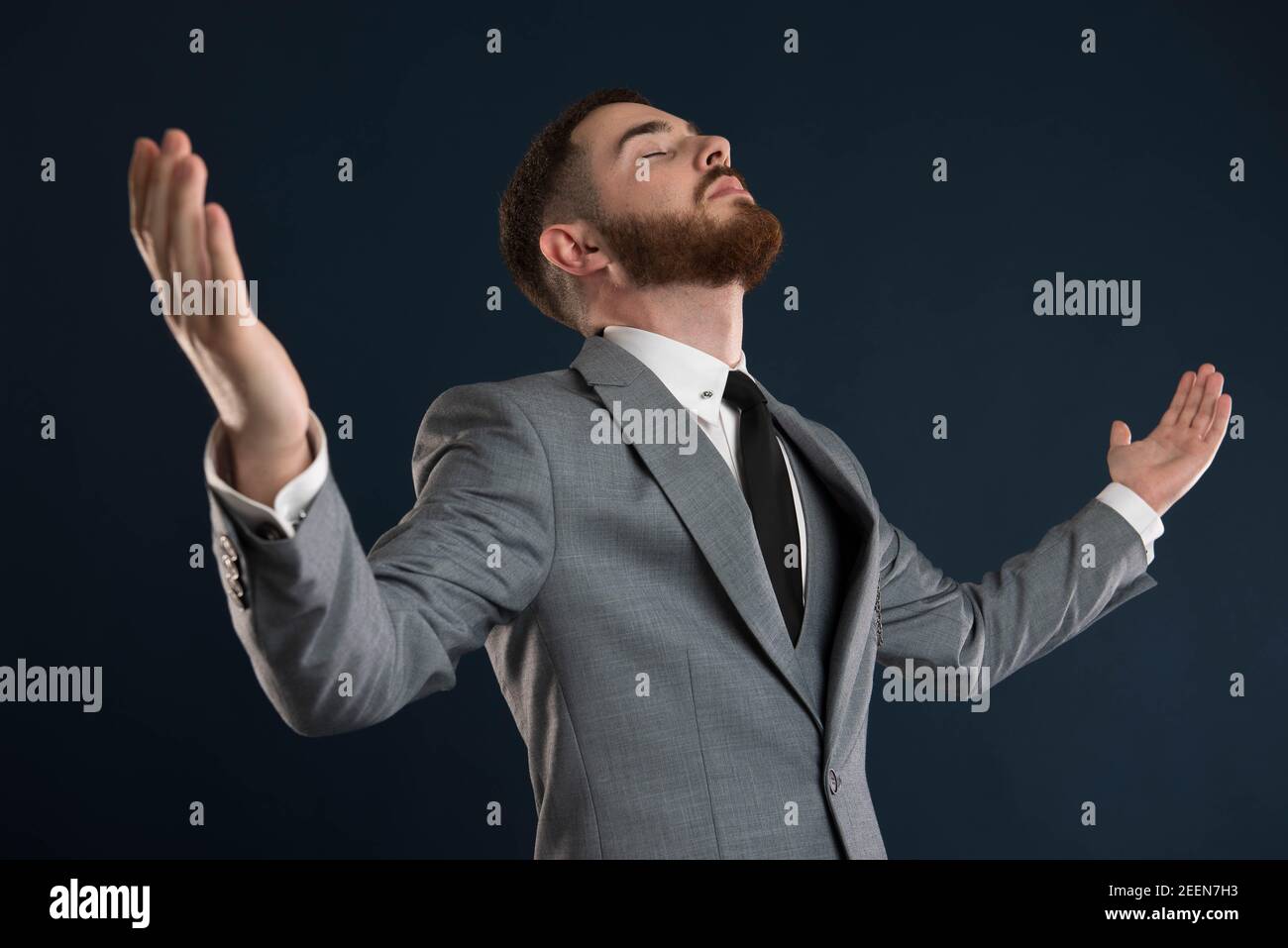 Young businessman raising his arms to the sky wearing a grey suit and black tie Stock Photo