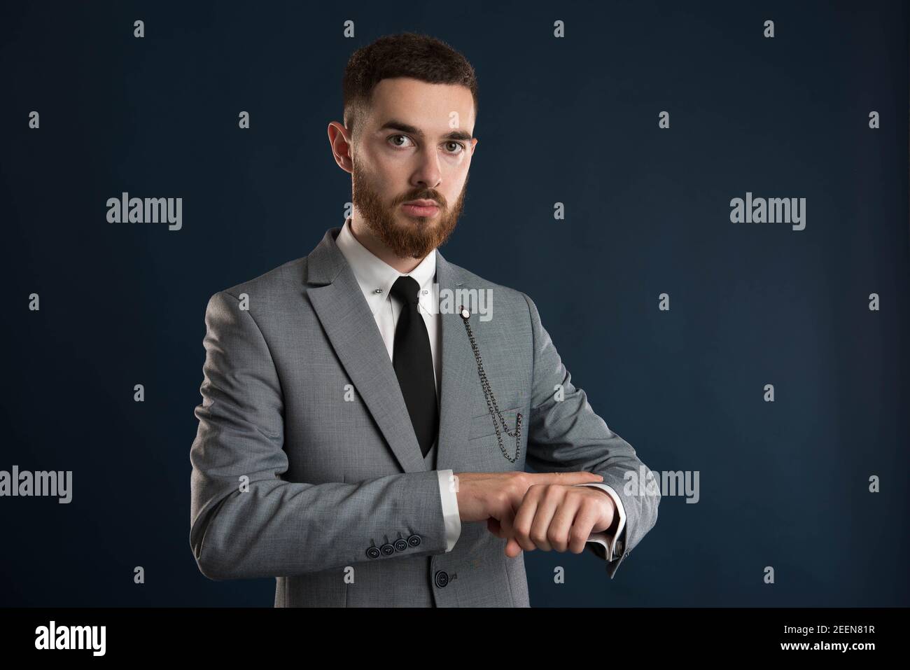 Upset young businessman checking the time wearing a grey suit and black tie Stock Photo