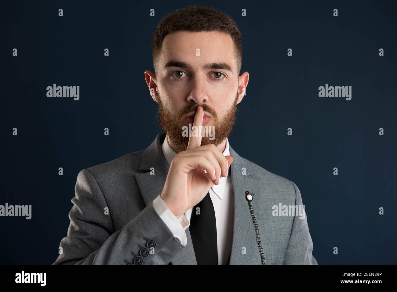 Young entrepreneur asking for silence wearing a grey suit and black tie and a beard Stock Photo
