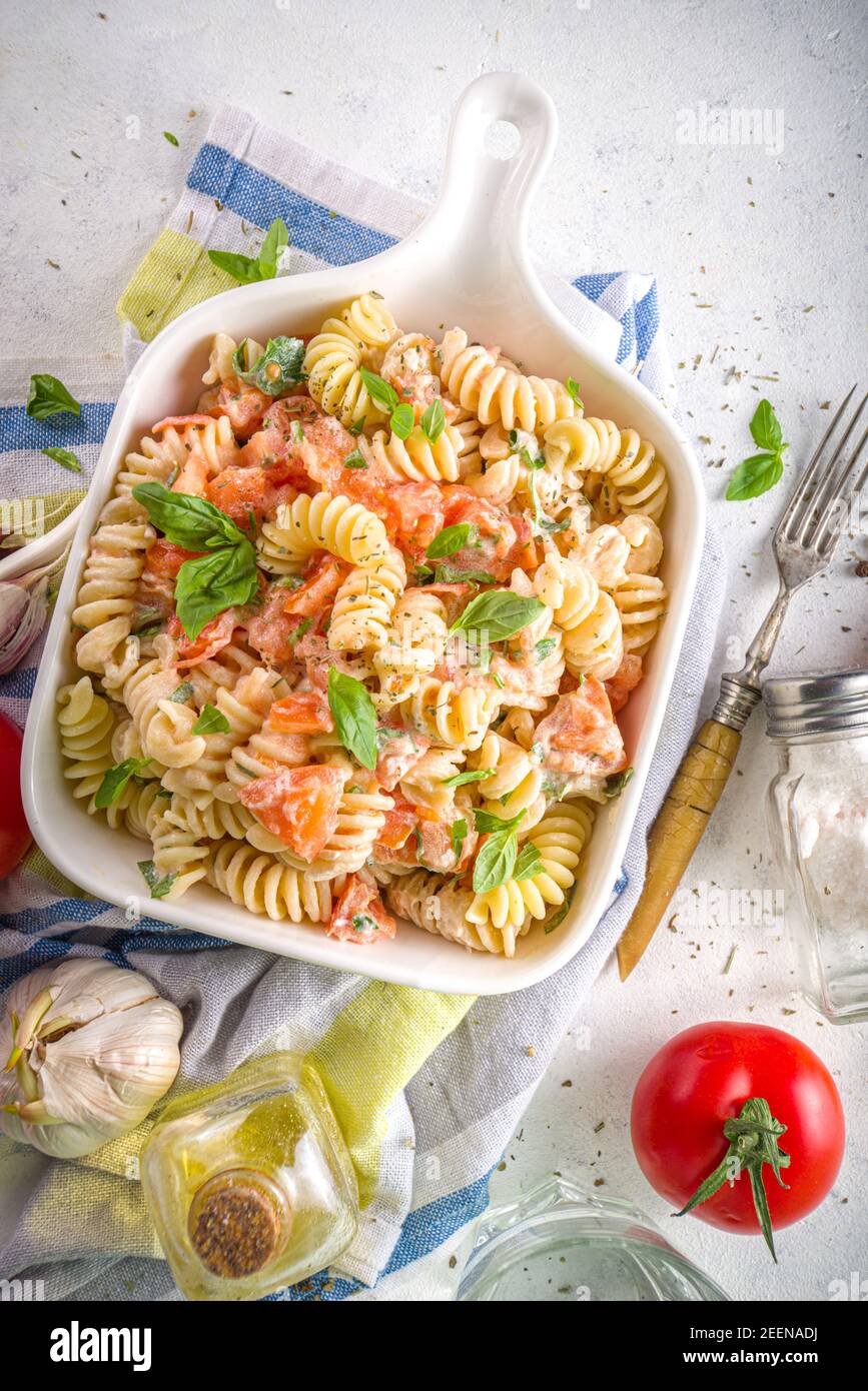 Spring diet healthy vegan pasta. Italian fusilli pasta with tomatoes, green vegetables, fresh herbs, cream cheese or feta, on white table background c Stock Photo