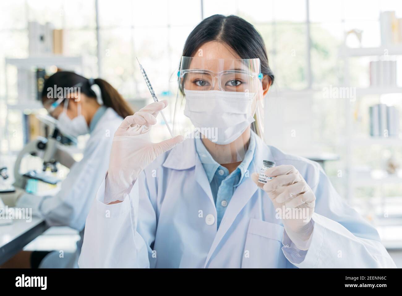 Successful young female medical researcher and scientist wearing labcoat standing in laboratory while working on developing covid-19 vaccine holding injection and bottle Stock Photo
