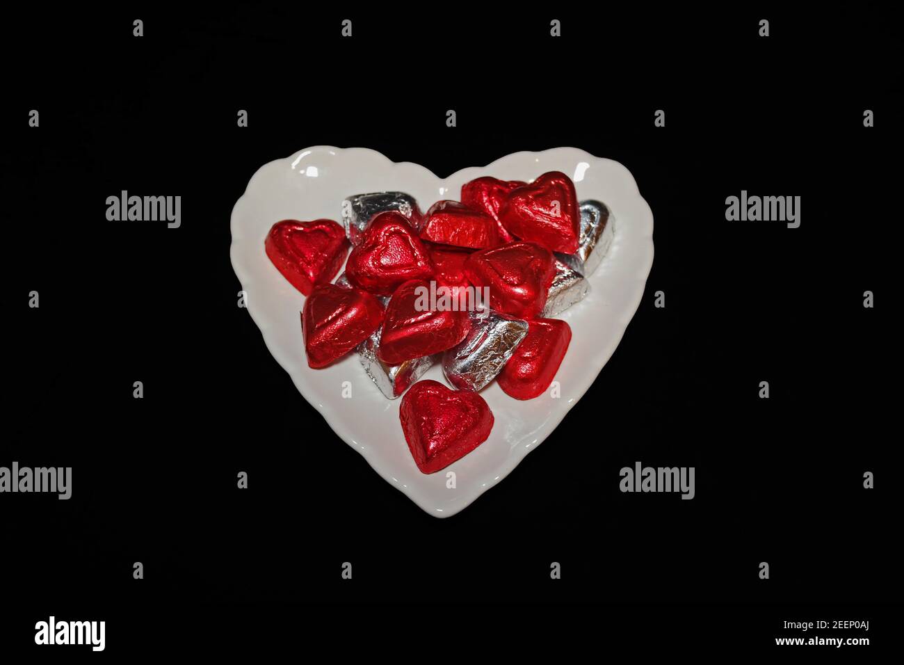 Foil Covered Chocolate Hearts on White Plate on Black Background Stock Photo