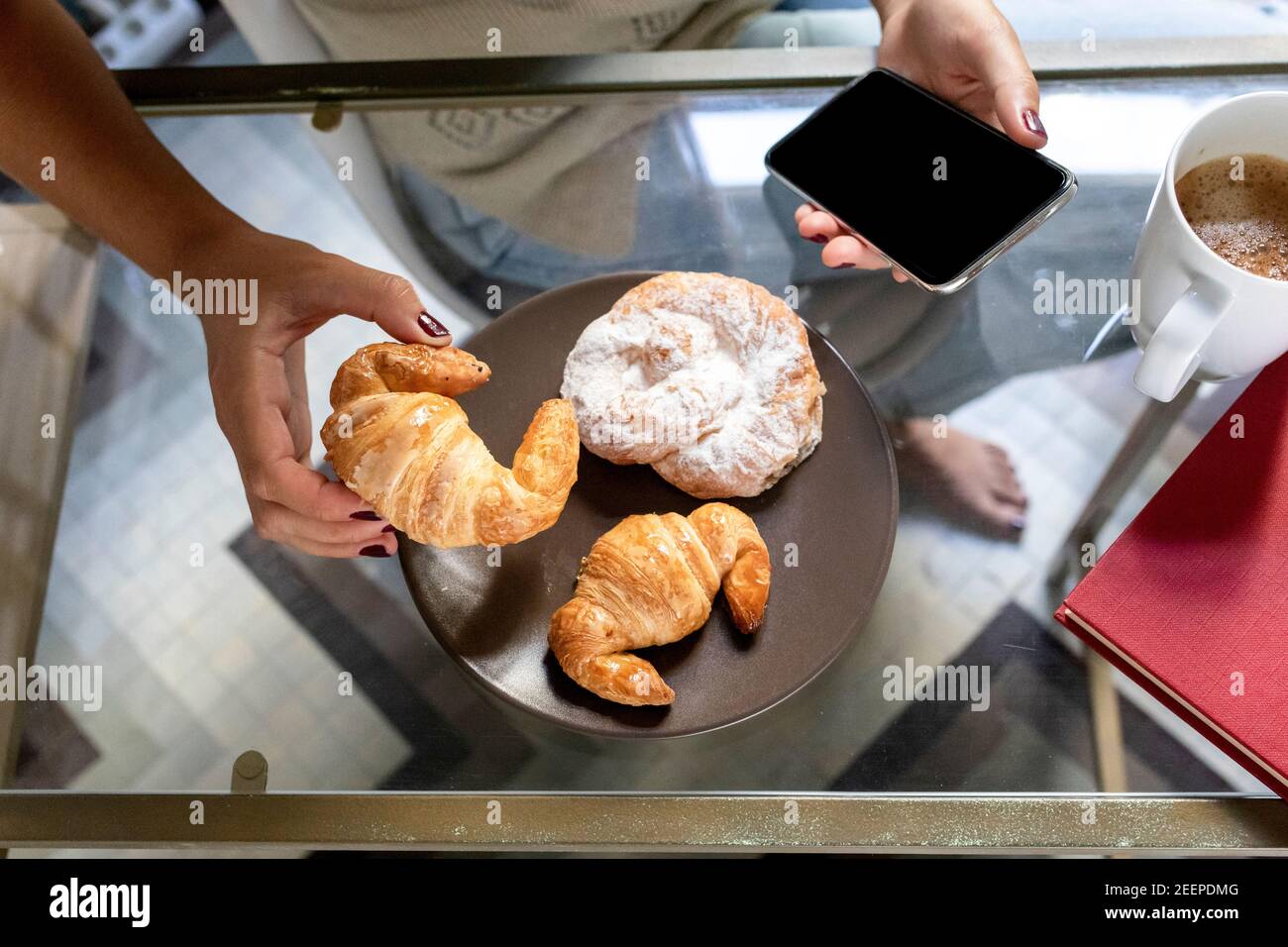 Detail of a girl eating breakfast with her cell phone in her hand Stock Photo