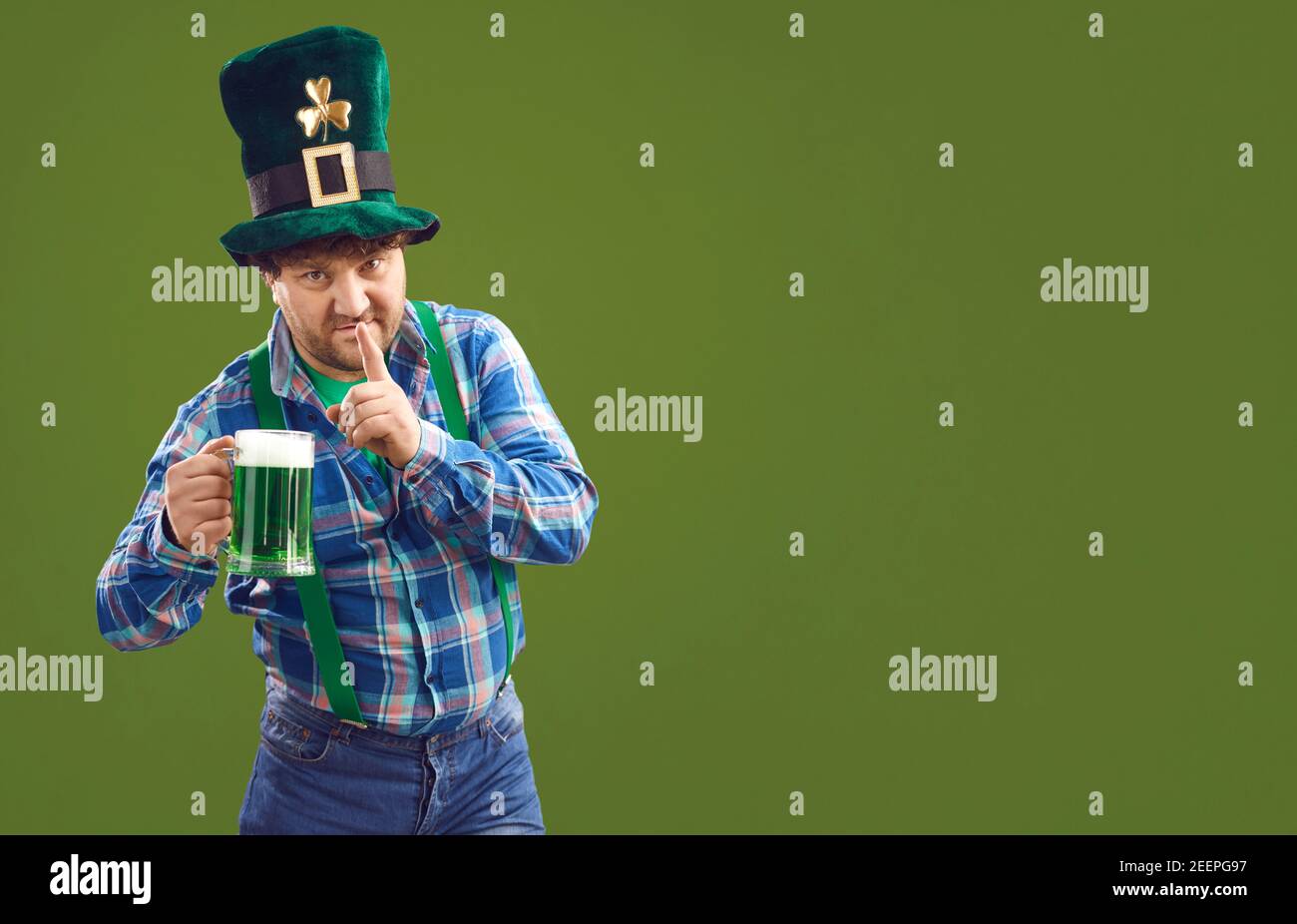Positive man standing with green beer and showing silence sign for Patrick day Stock Photo