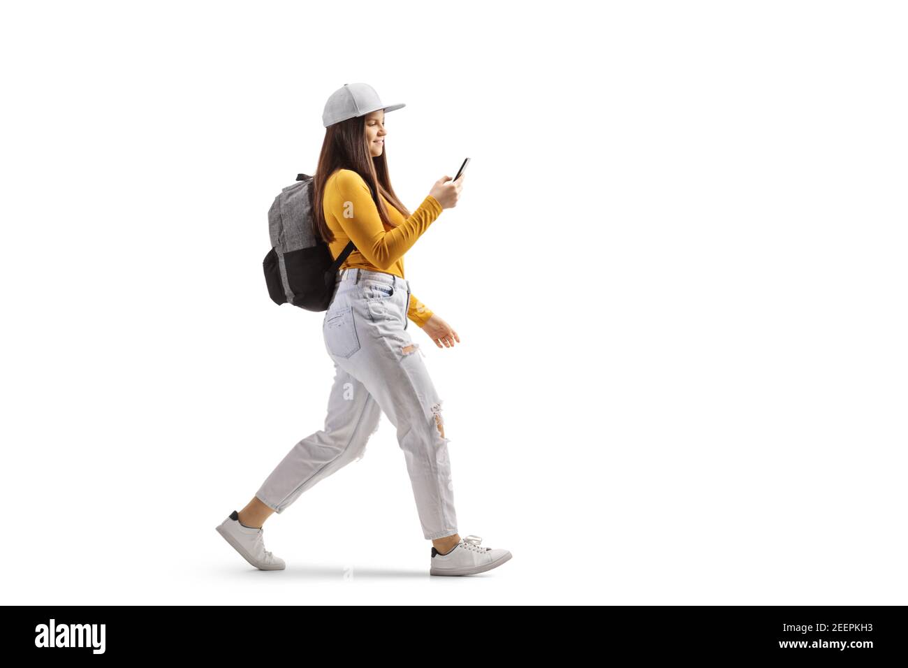 Full length profile shot of a female student walking and typin on a mobile phone isolated on white background Stock Photo