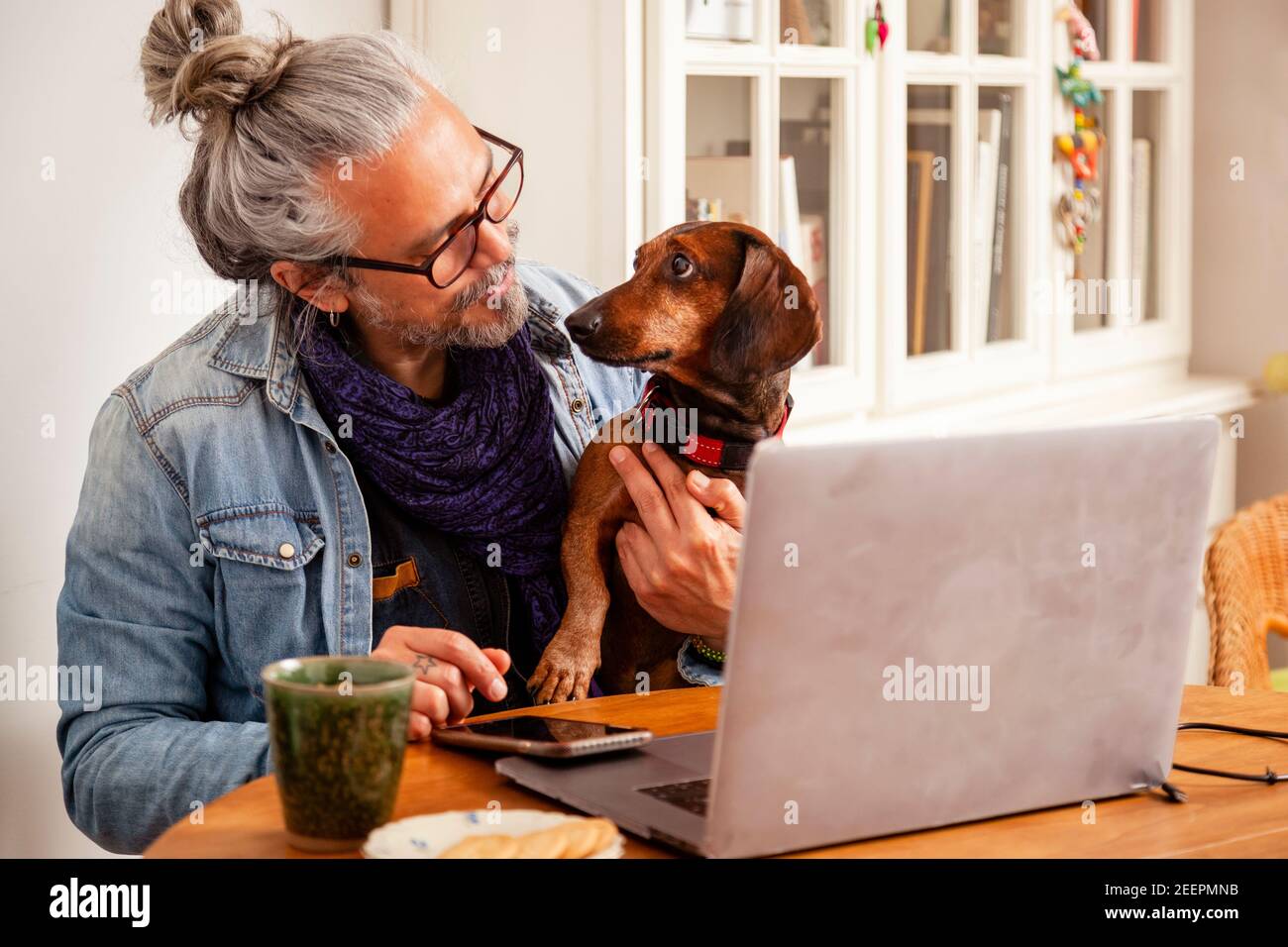 Handsome man working at home with laptop on the table together with his cute dog; concept: close relationship of dog and human Stock Photo
