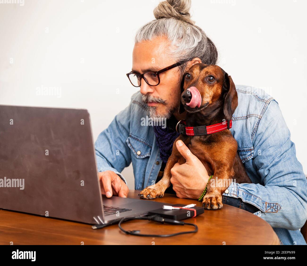 Handsome man working at home with laptop on the table together with his cute dog; concept: close relationship of dog and human Stock Photo