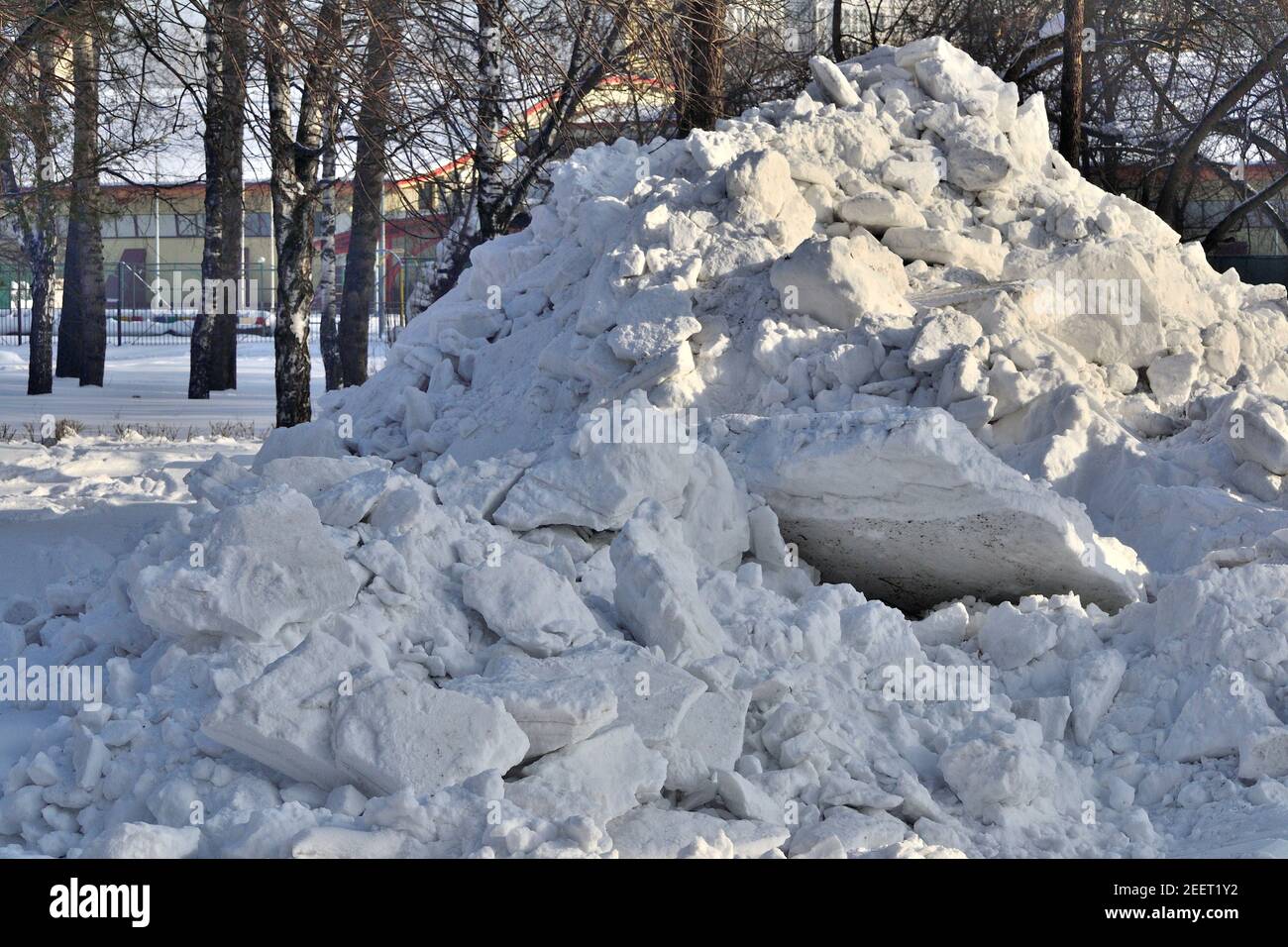 Snowdrift in the city park. Municipal communal services are cleaning snow on roads and alleys of city park. High snowdrift after snowfall or blizzard Stock Photo