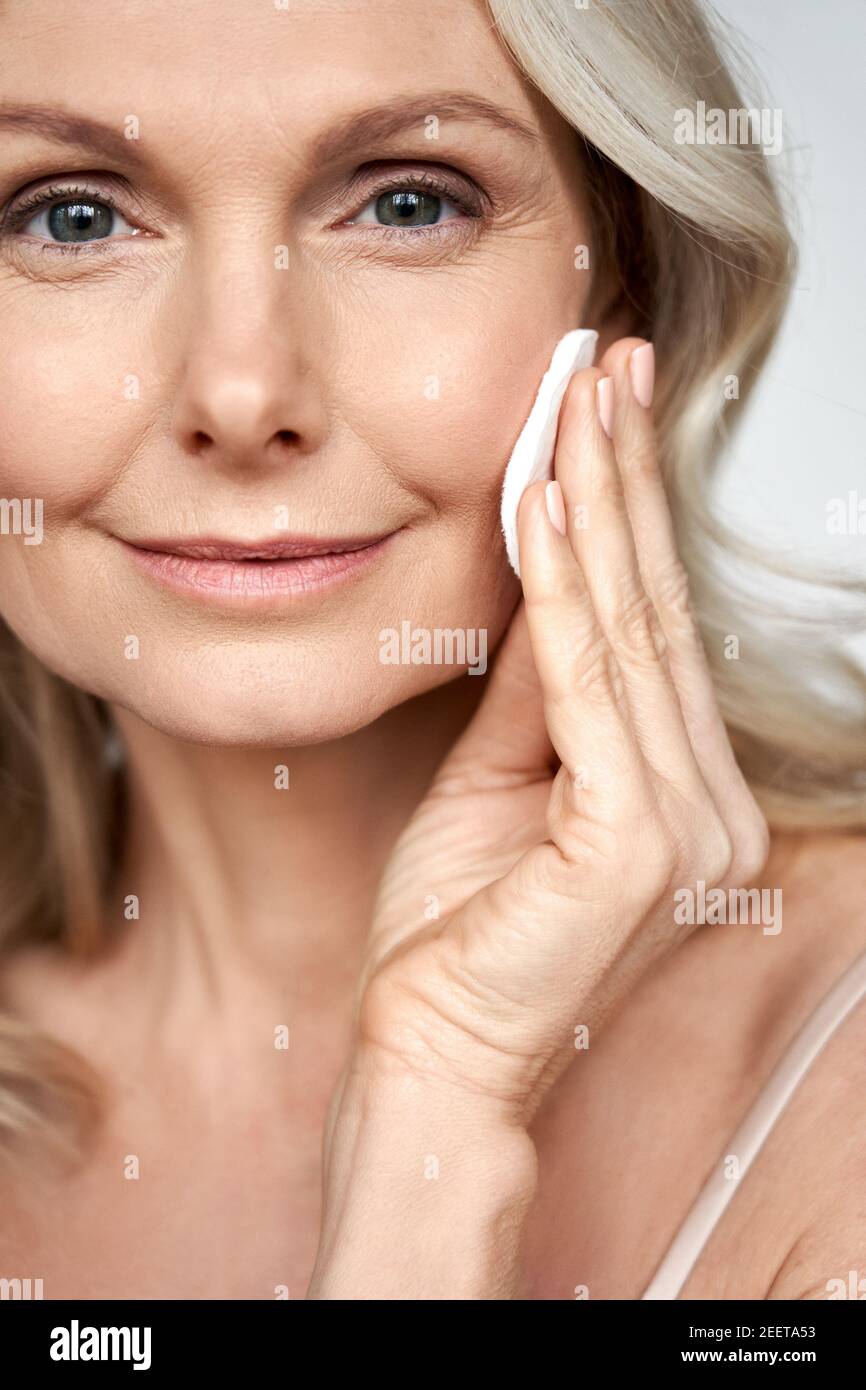 Pretty 50s middle aged woman holding cotton sponge cleaning face skin. Stock Photo