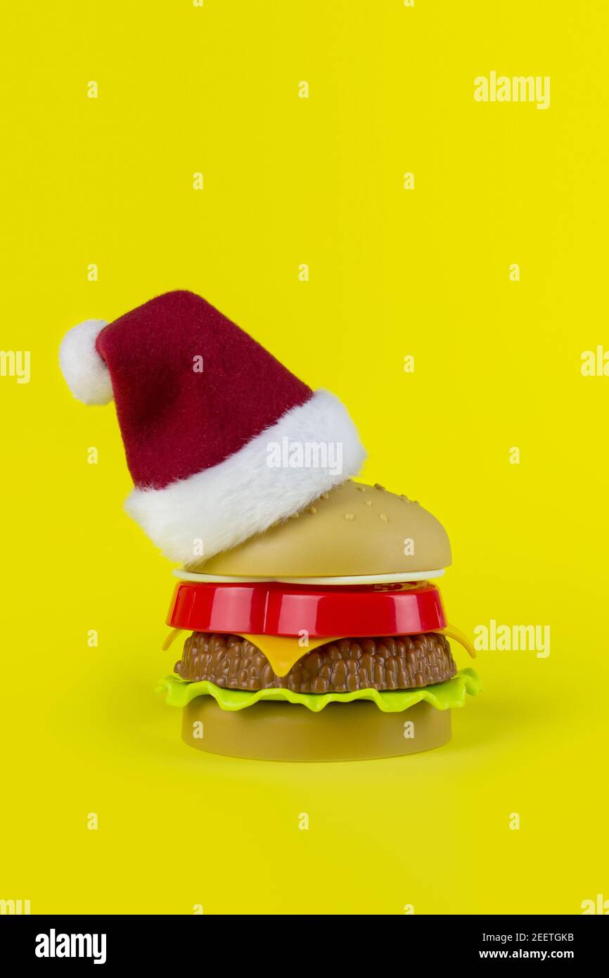 Santa's red hat on Plastic hamburger in form christmass tree on yellow background. Santa Claus loves to eat fast food Stock Photo