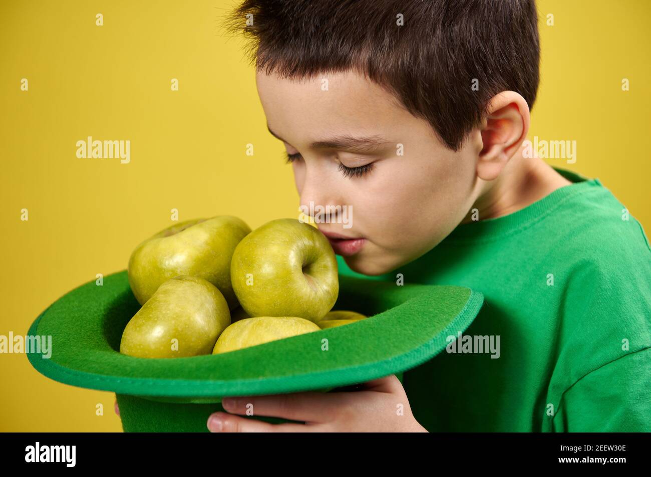 Little cute boy enjoys the scent of green apples in a green Irish leprechaun cap. Face portrait. Saint Patrick's Day Stock Photo