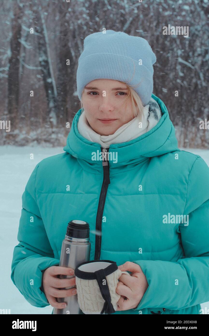 Girl teenager 15 years old on walk in winter woods holding thermos and mug of hot tea. Picnic in frosty snow. Stock Photo