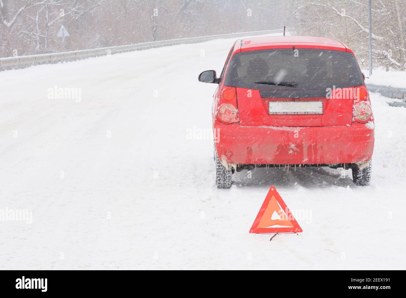 Broken car on snowy road. Red triangle warning sign for emergency stop. Snow and blizzard, winter driving hazard. Stock Photo