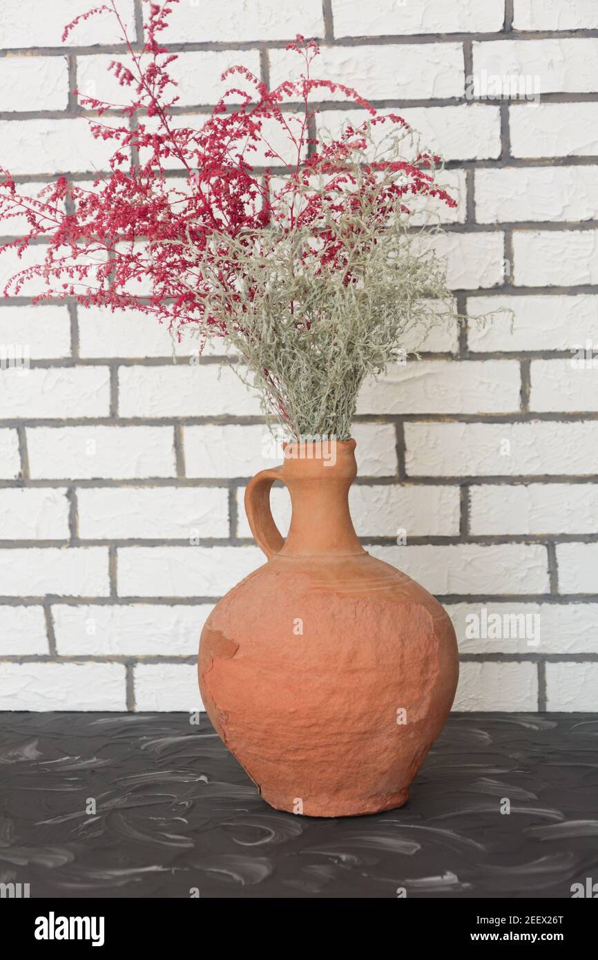Antique brown clay jug with dry grass branches in home interior. Ancient traditional craft. Stock Photo