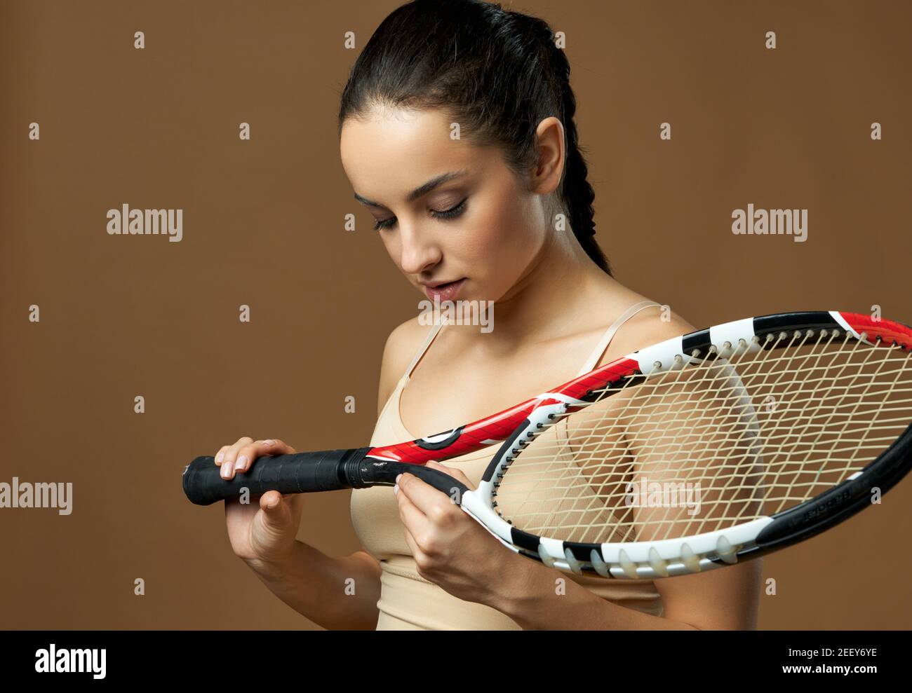 Attractive brunette lady looking at tennis racket in her hands with serious expression. Isolated on beige background Stock Photo