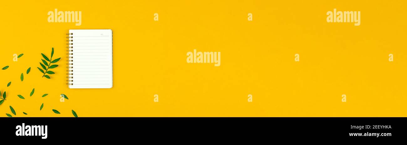 Springn mockup on yellow background with blank notepad in lines, green leaves, flat lay banner, copy space, workspace Stock Photo