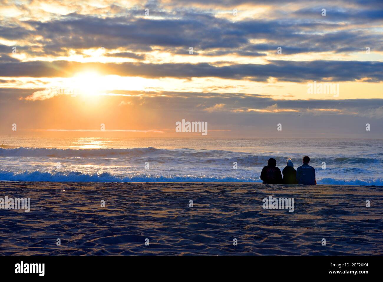 3 Friends sitting on the beach at sunrise facing East for an Atlantic Ocean sunrise in NJ Stock Photo