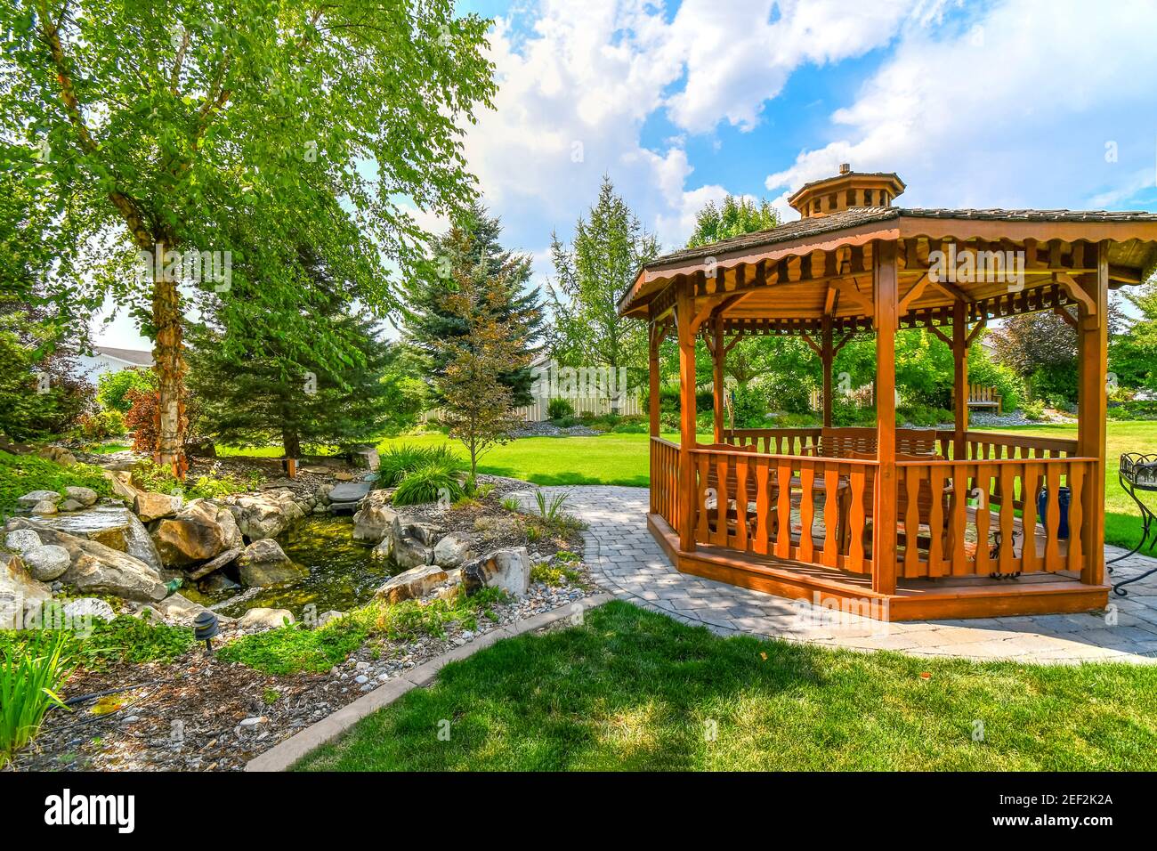 A nicely landscaped garden and back yard with a round wooden cedar gazebo  and a pond with waterfall Stock Photo - Alamy