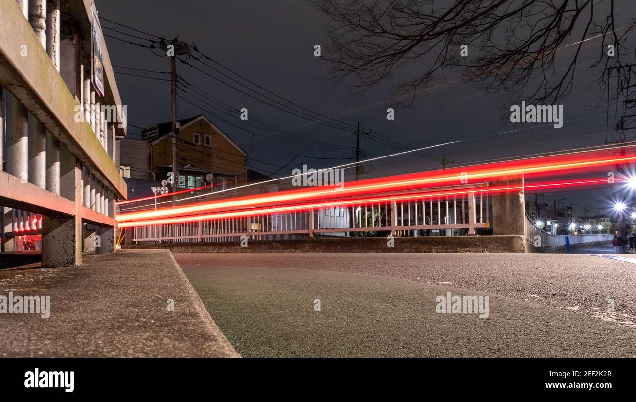 A light trail image of a car crossing a bridge at night in suburban Tokyo. Stock Photo