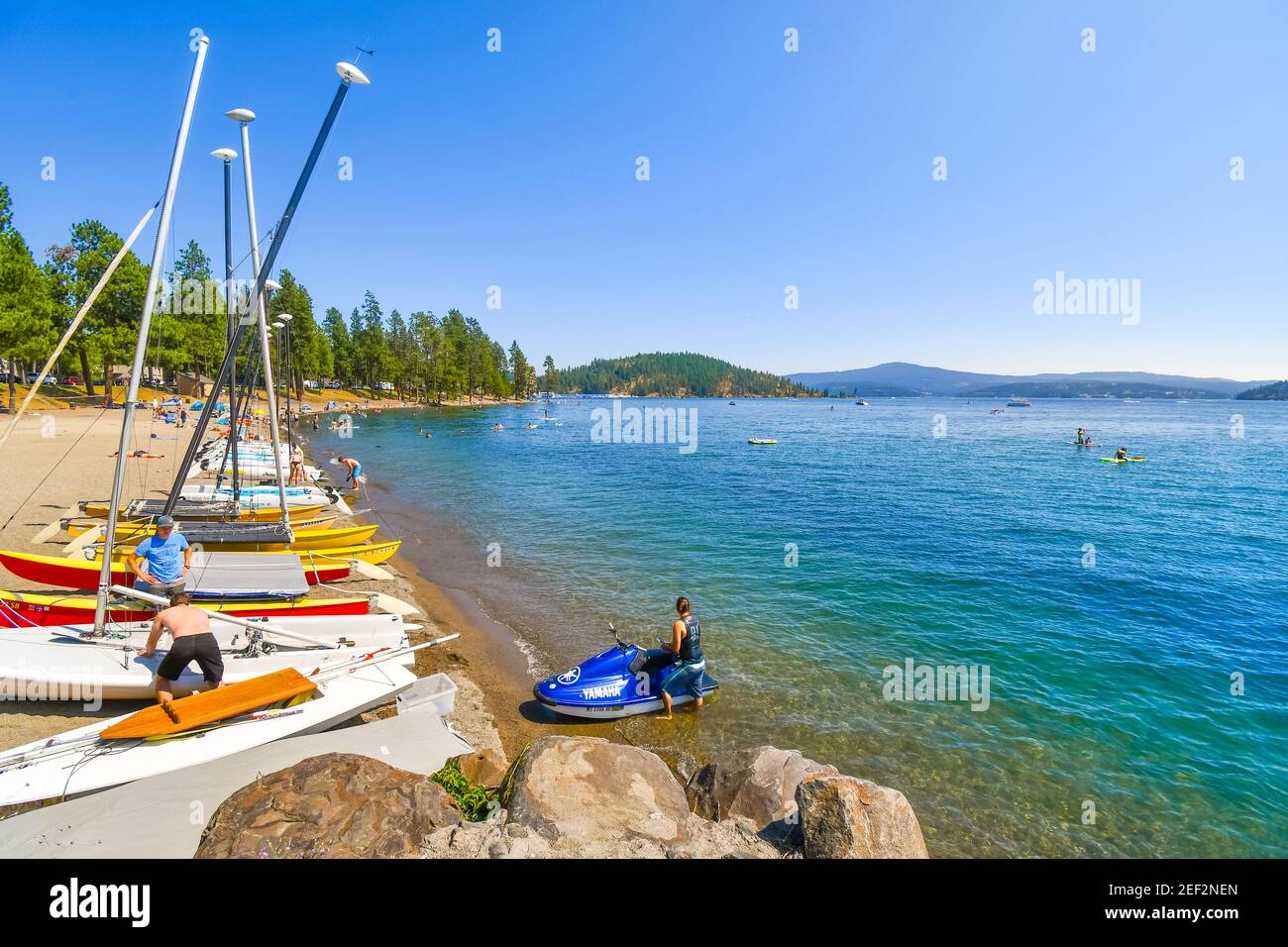 A young man on a wave runner jet ski stands on the beach next to boats