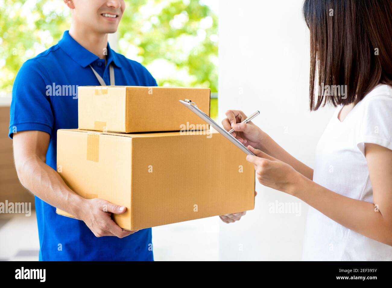 Woman signing document, receiving parcel box from delivery man - courier service concept Stock Photo