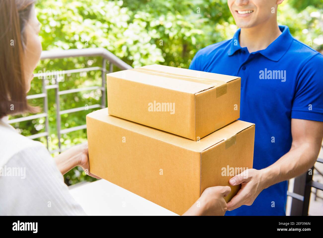 Delivery man in blue uniform handing parcel boxes to a woman - courier service concept Stock Photo