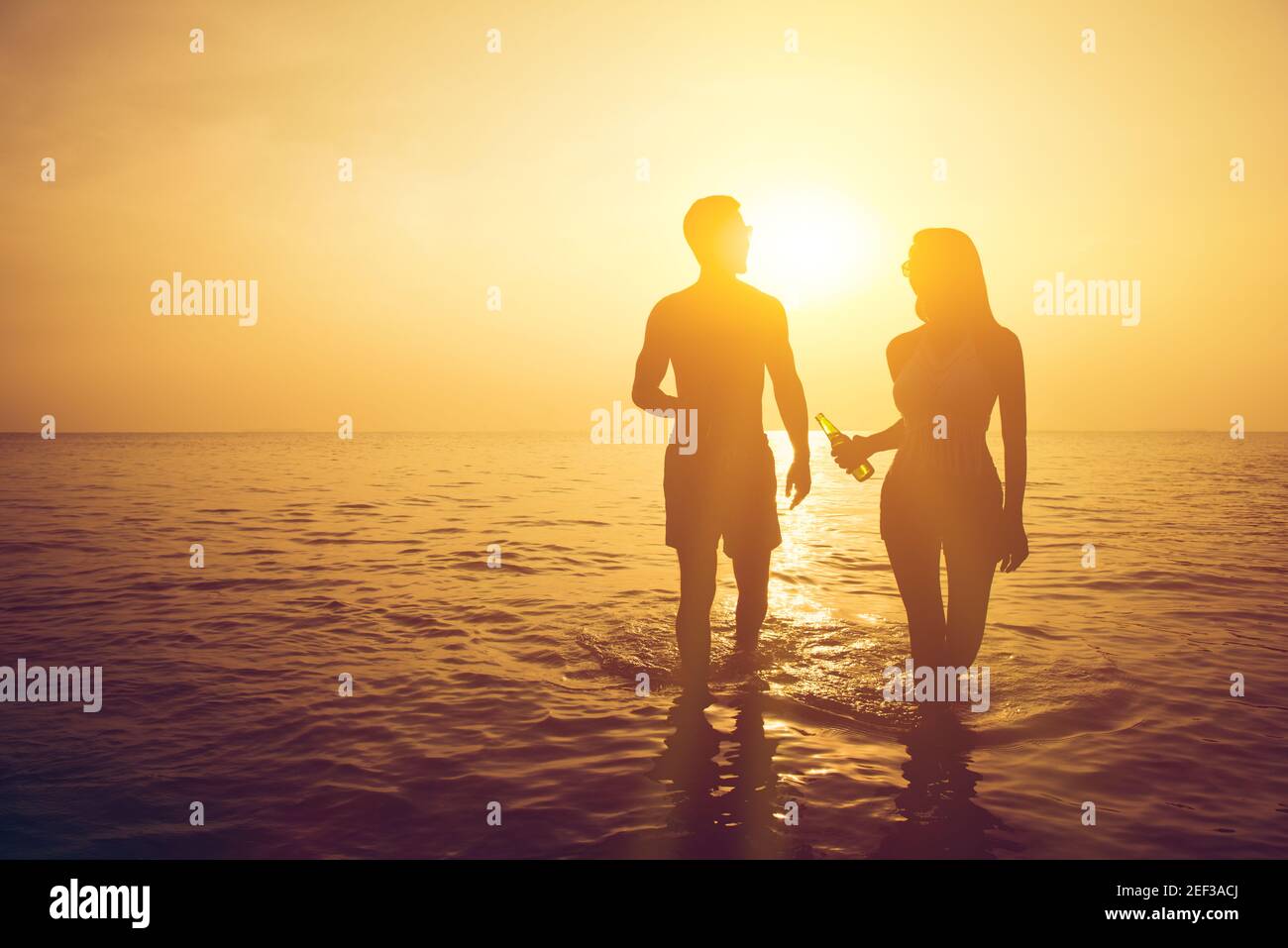 Silhouette of couple walking in seawater at the beach in twilight ...