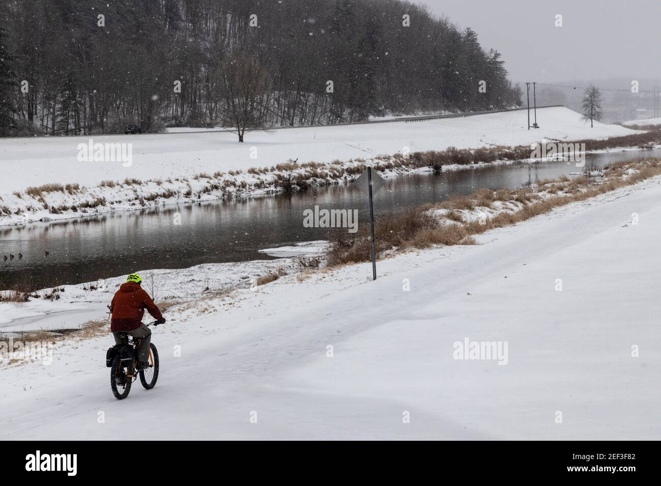 A man rides a bike near the Hocking River during a snowstorm.Snowstorm Uri swept across the United States from February 12th to the 16th covering the United States in snow and Ice. Uri begun in the Pacific Northwest, and headed all the way to the southeast of US. The storm has claimed many lives due to car accidents and low temperatures. In Athens County Ohio the storm began on Monday morning February 15, 2021 and has continued into Tuesday 16, 2021. Currently Athens County is under a level two snow emergency. Stock Photo