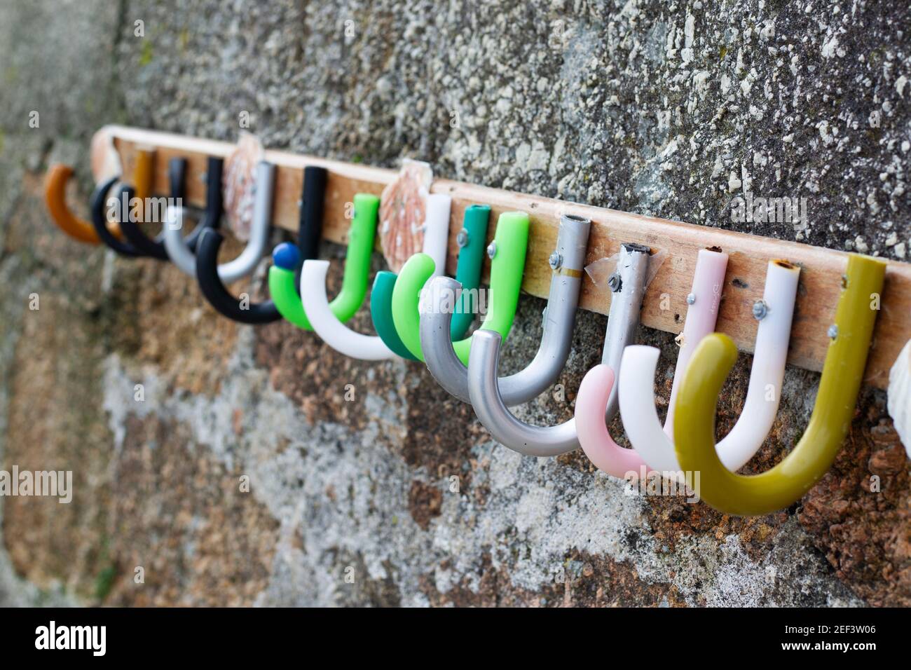 clothes hanger made up of different colored umbrella handles placed on the entrance wall to a beach Stock Photo