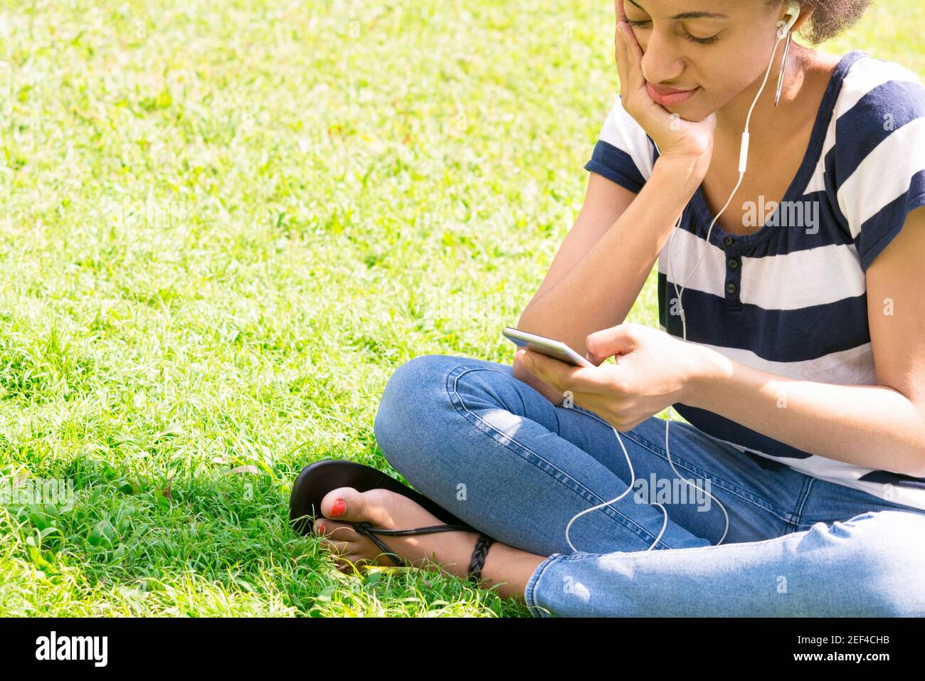 Casual woman sitting on the grass and listening to music from smartphone Stock Photo