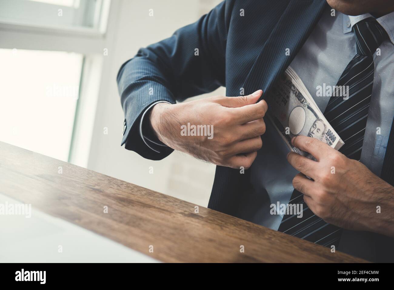 Businessman putting money, Japanese  yen banknotes, into his suit pocket - bribery and corruption concept Stock Photo