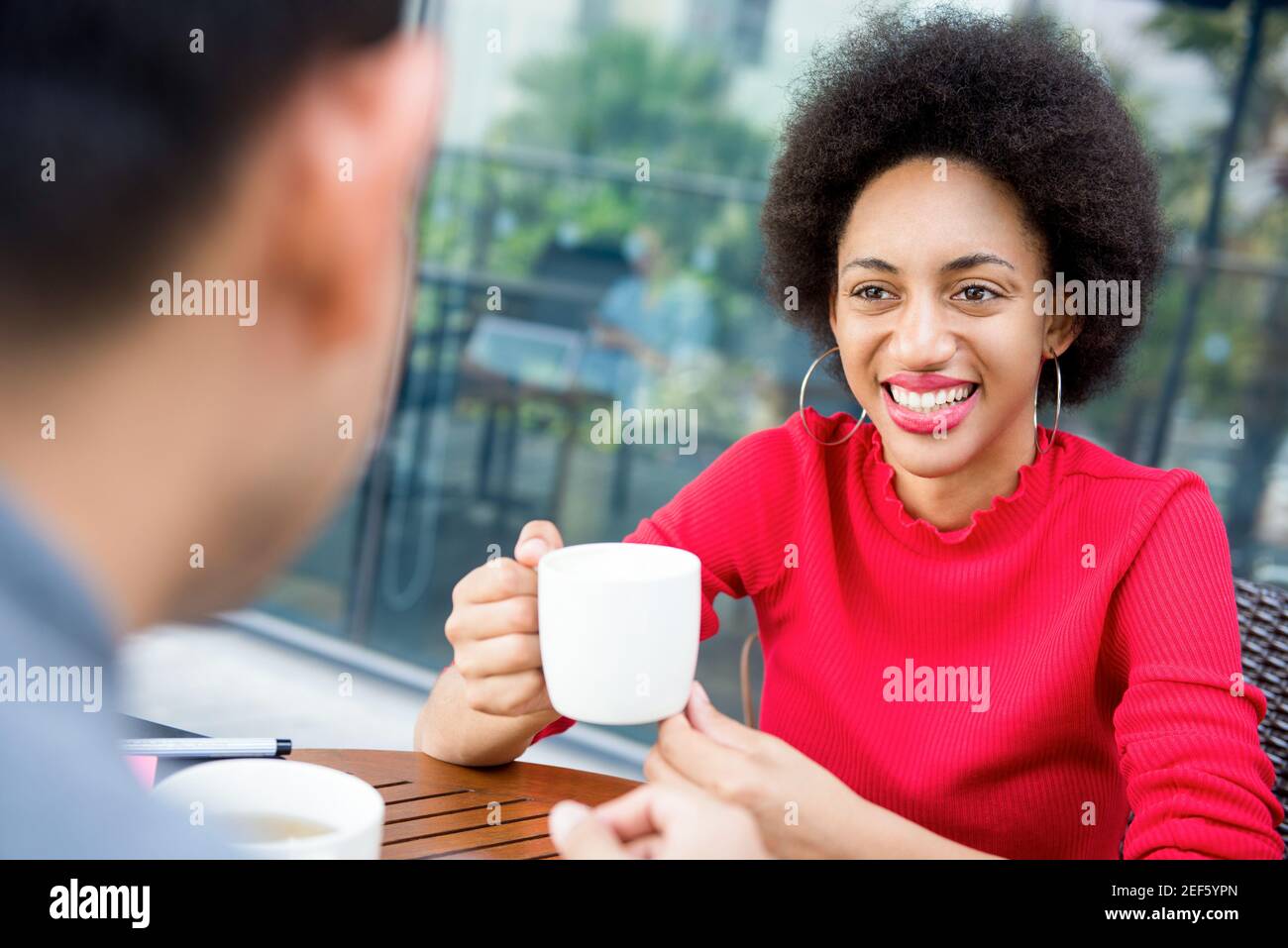 Smiling casual Afro-Caribbean woman drinking coffee with a friend in coffee shop Stock Photo