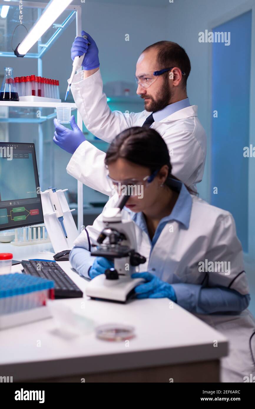 Scientist examining blood sample looking under microscope while chemist