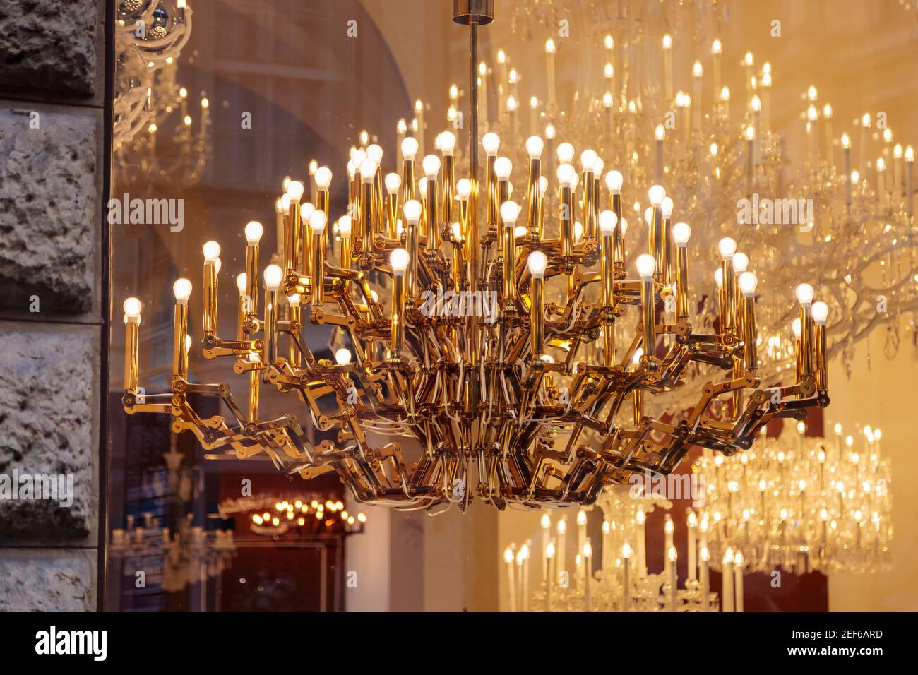 Expensive luxury large chandelier behind glass with gilding. Reflection in the shop window. Lights in the form of candles. Stock Photo