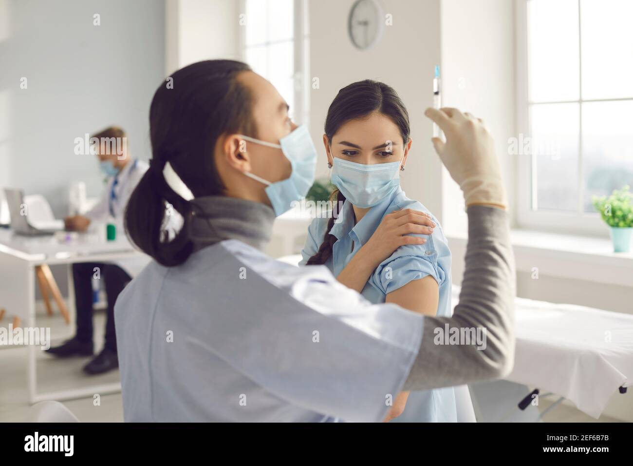 Young woman in medical face mask getting Covid-19 clinical trial vaccine at hospital Stock Photo
