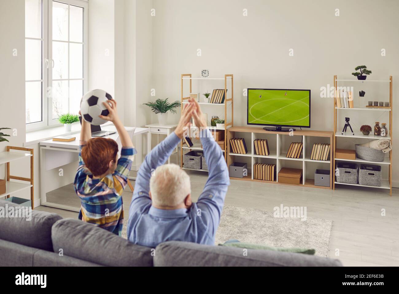 Grandpa and grandson sitting on couch, watching soccer and supporting favorite team Stock Photo