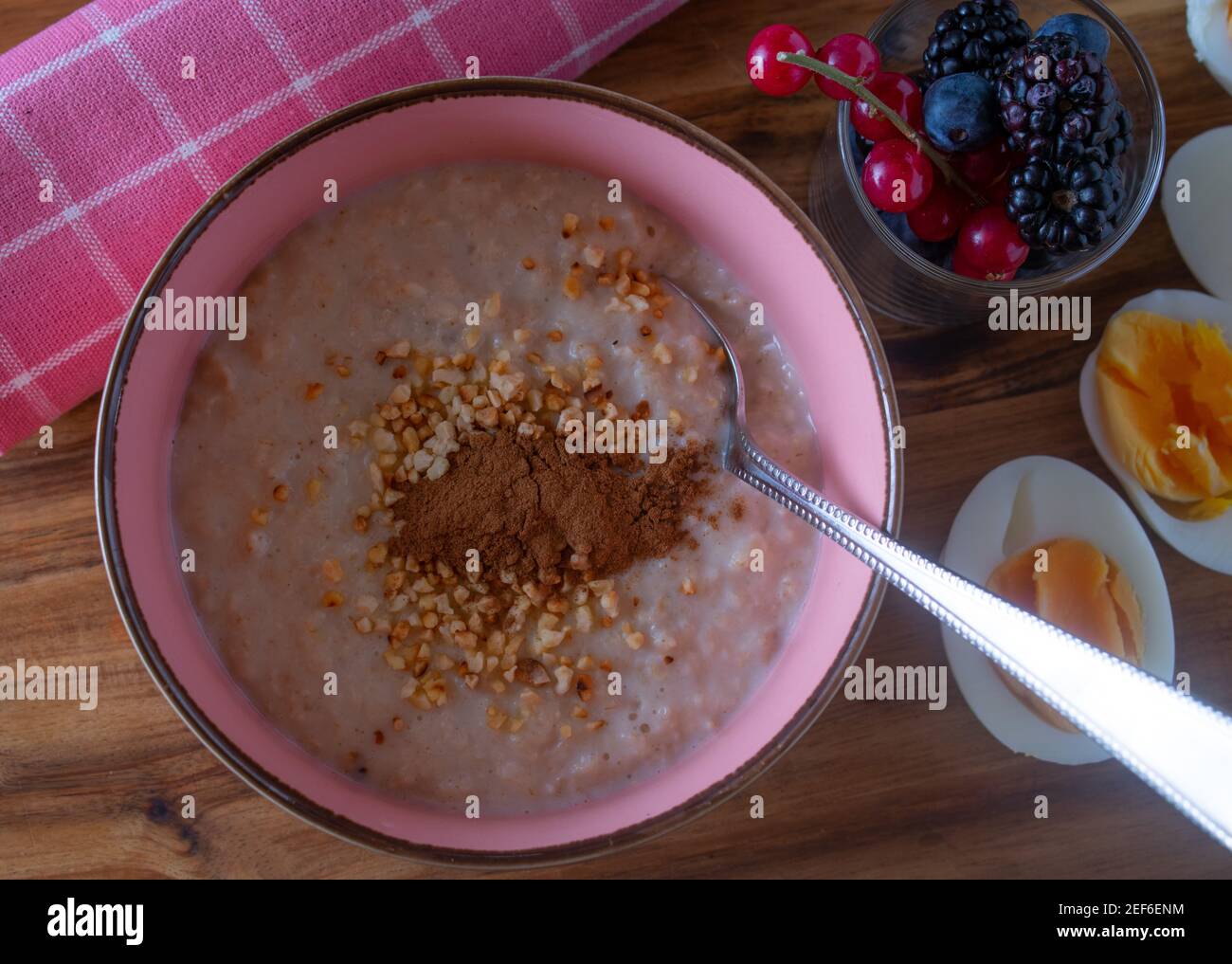 A bowl of fresh cooked porridge with roasted almonds and cinnamon served with a glass of fresh berries and boiled eggs Stock Photo