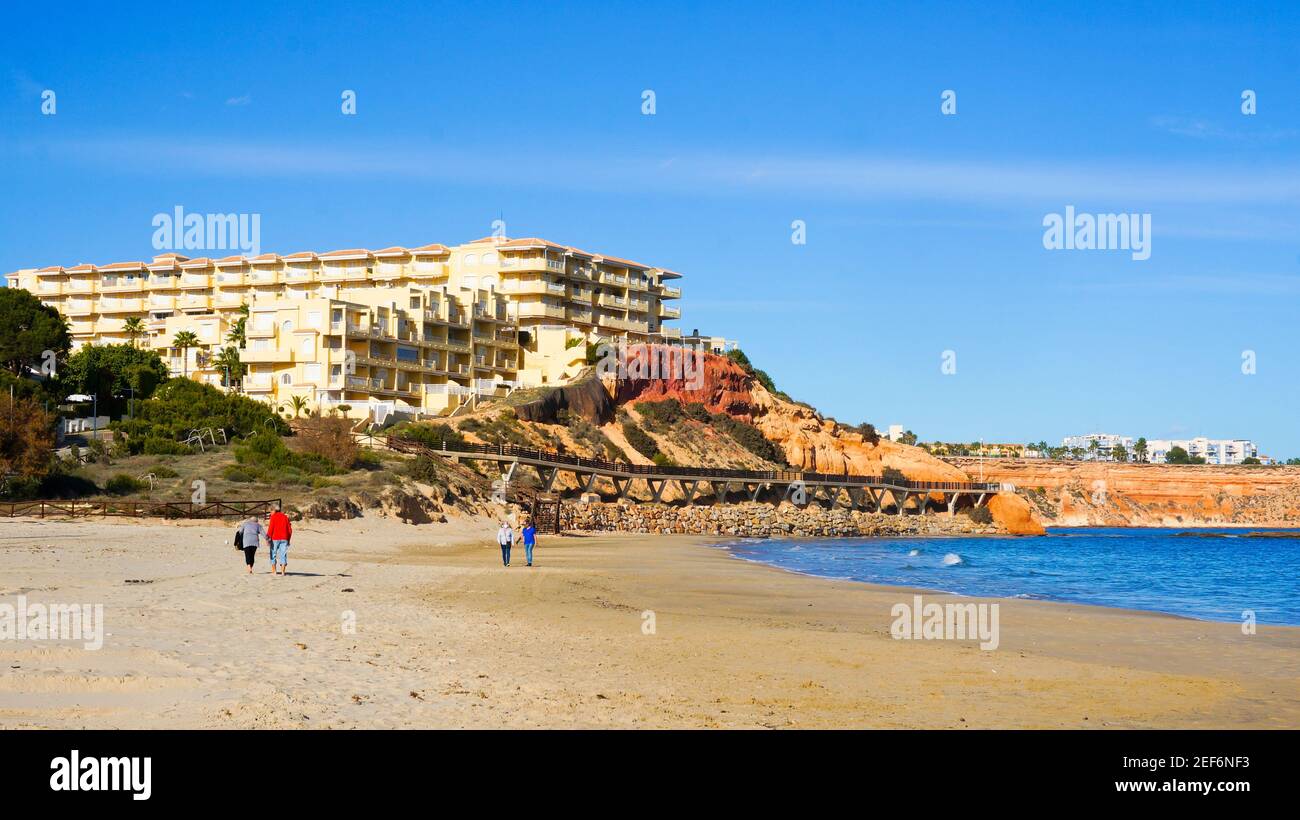 Alicante, Orihuela Costa, Spain - February, 2021: People having a walk on lovely sunny day by the Campoamor beach on weekend  Stock Photo