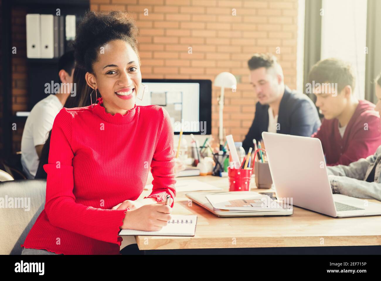 Casual Caribbean business woman in meeting room of   interior design company with multiethnic colleagues Stock Photo
