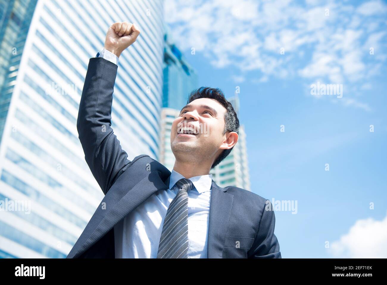 Businessman smiling and raising his fist in the air in office building background - business success and achievement concepts Stock Photo