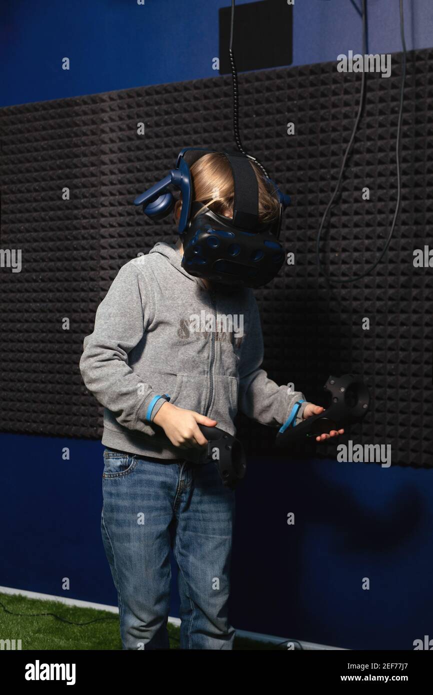6 year old boy in virtual reality helmet is learning how to control game using controllers. Stock Photo