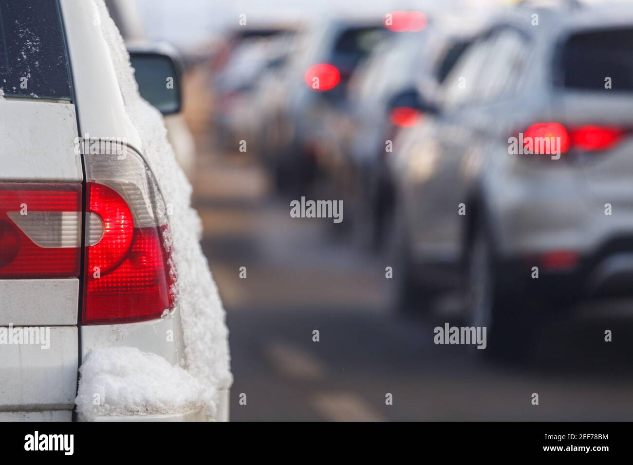 white car tail light with snow and blurry traffic in the background at winter day. Stock Photo
