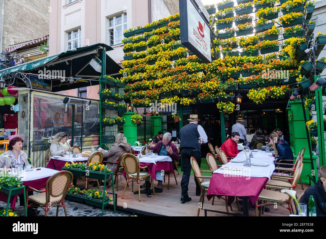 Flowers in pots on historic place Skadarlija with trees, cafes, cobbled lanes and alleys in downtown. Belgrade street with bars and restaurants. Stock Photo