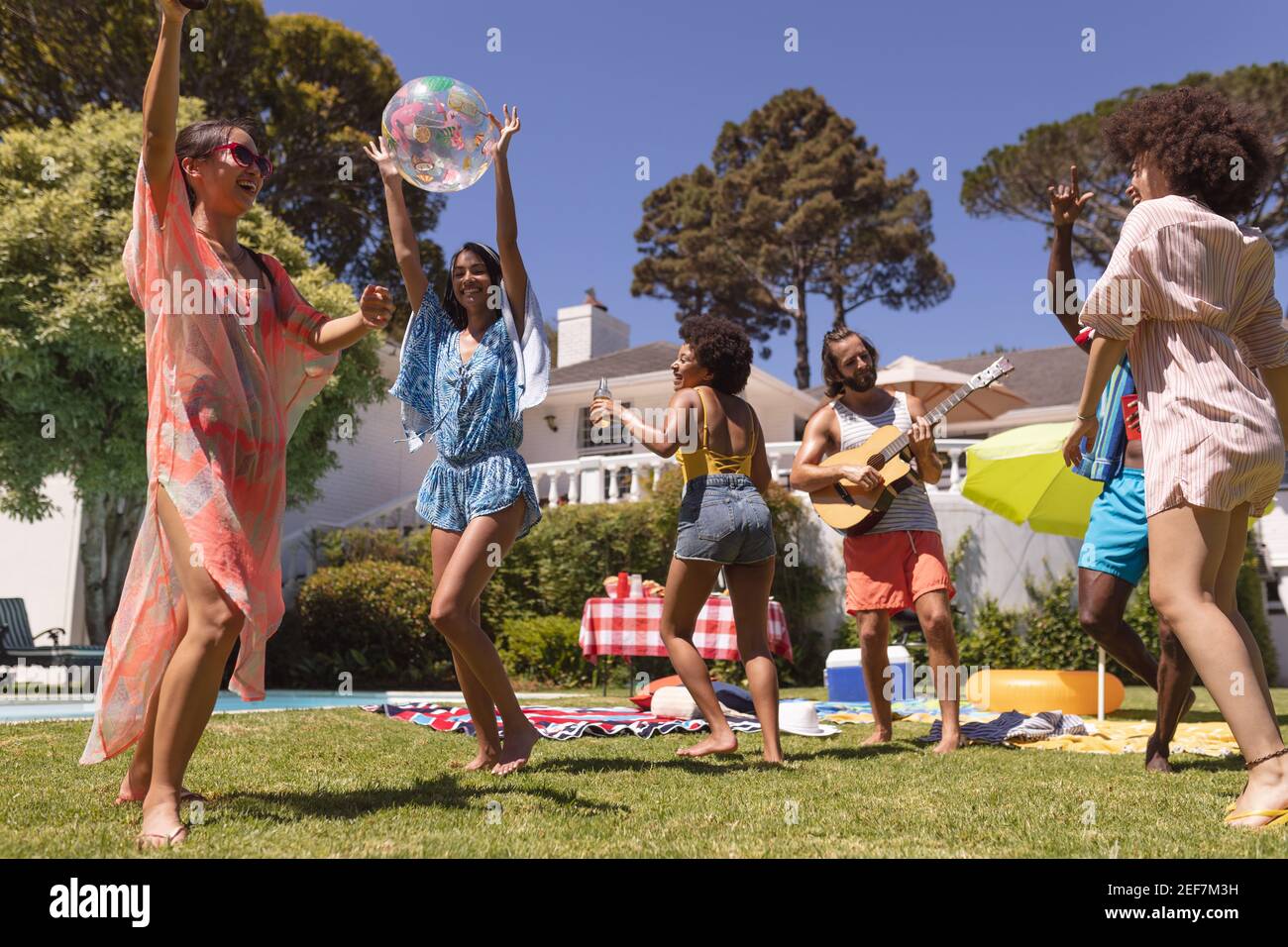 Diverse group of friends dancing and smiling at a pool party. Hanging out and relaxing outdoors in summer. Stock Photo