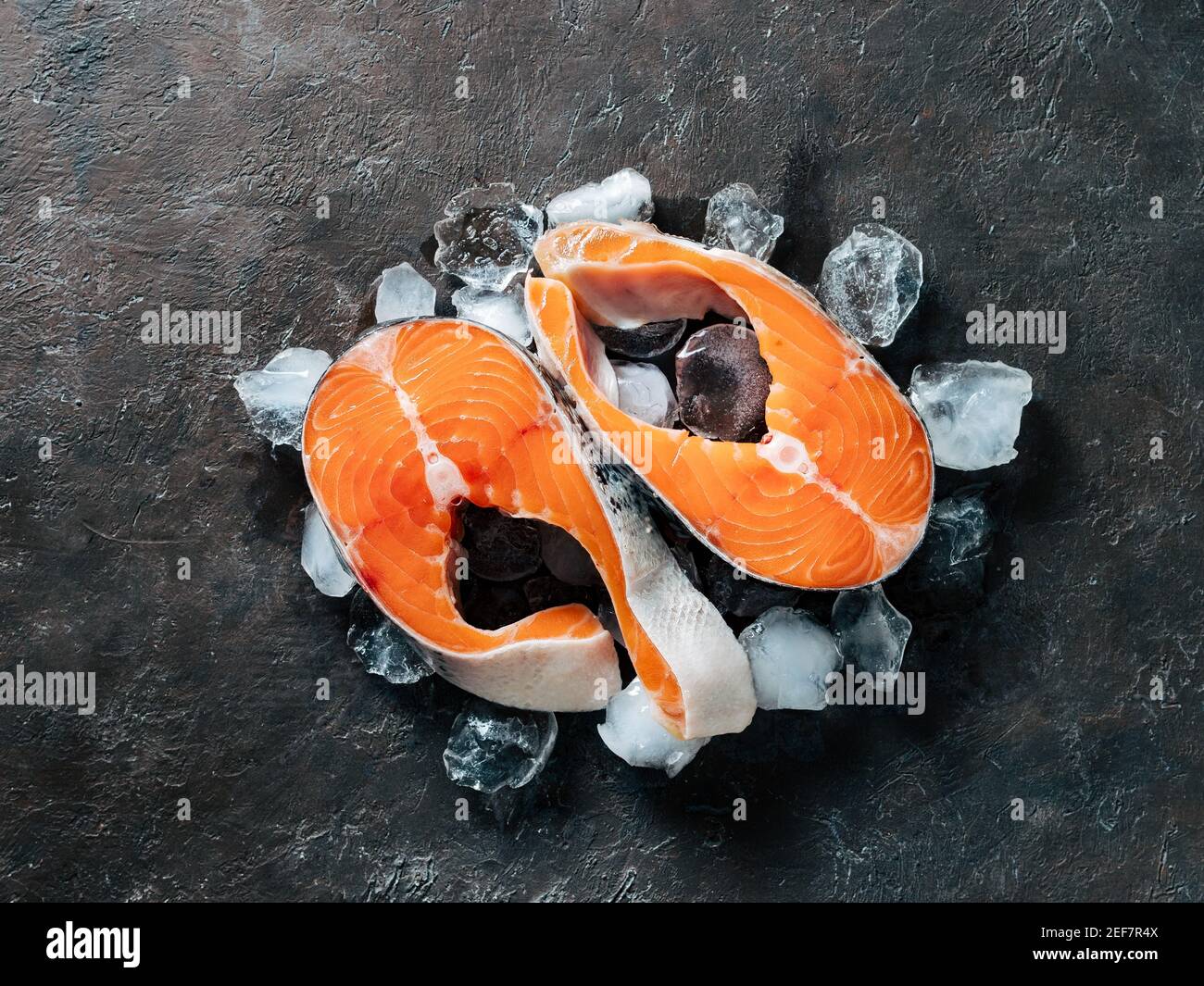 Two raw wild salmon steaks on ice over black textured background ...