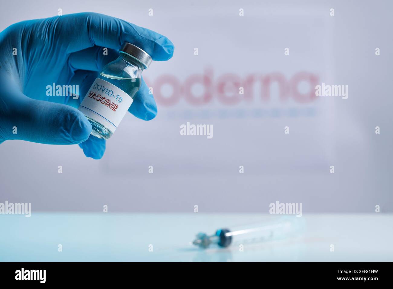 Coronavirus vaccine bottle held by a gloved hand and in the background the brand of pharmaceutical companies pfizer and modern Stock Photo