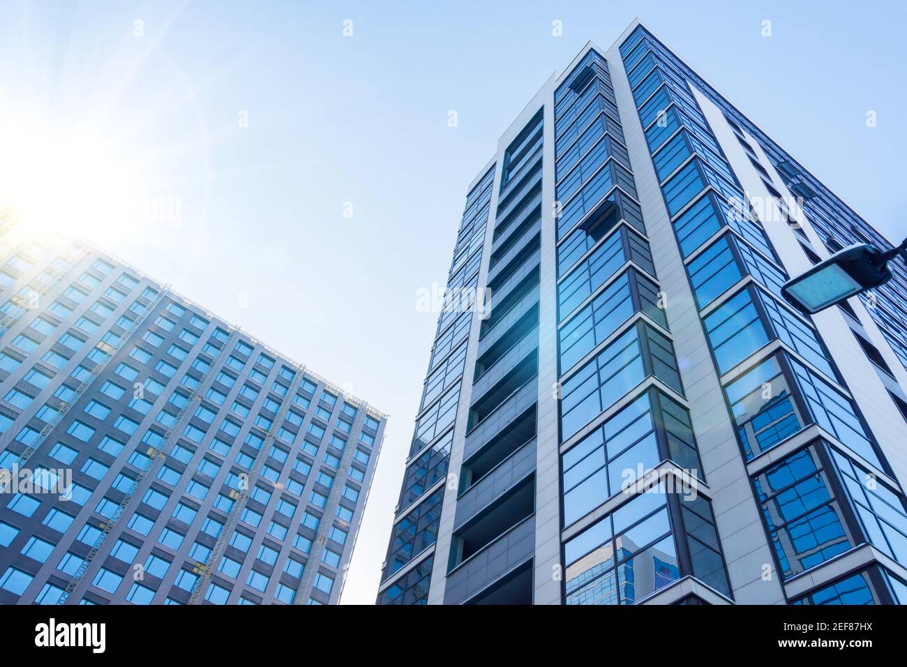 Multi-storey buildings with a glass facade and under construction with a facade department, with a bright sun in the sky Stock Photo