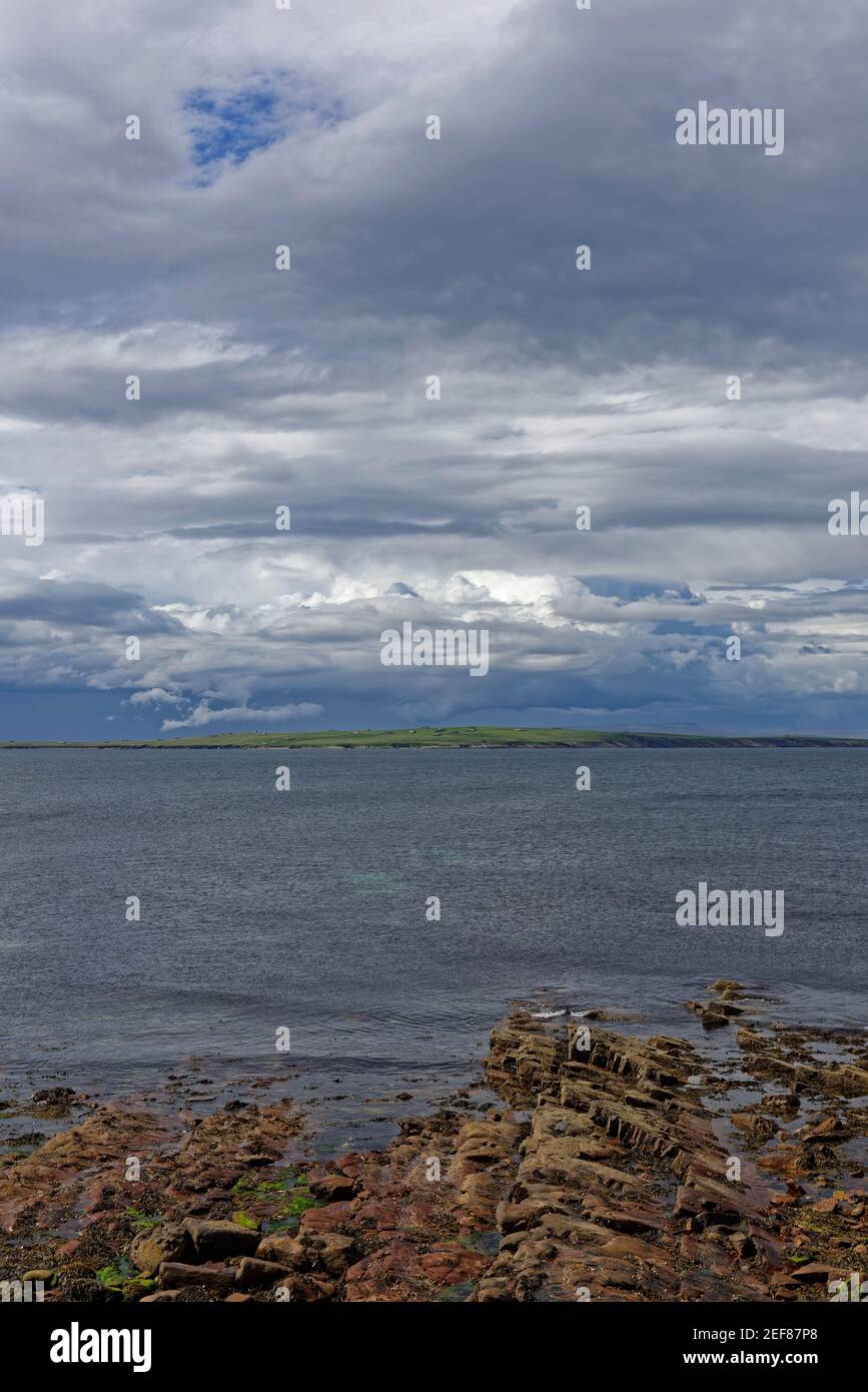 Looking across to the the island of Stroma, part of the Orkneys from the rocky beach at John OÕGroats with dark rain clouds on the horizon. Stock Photo